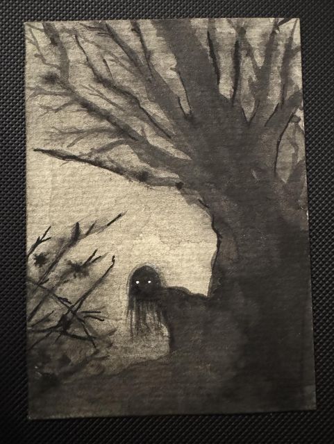 A grey and black forest landscape. The shadowy outline of a female figure with long black hair peers out from behind a tree without leaves. Only her eyes shine out of the darkness.