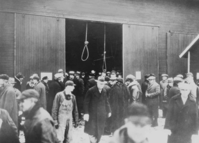 Men milling about in a front of a barn, two nooses hang from the rafters