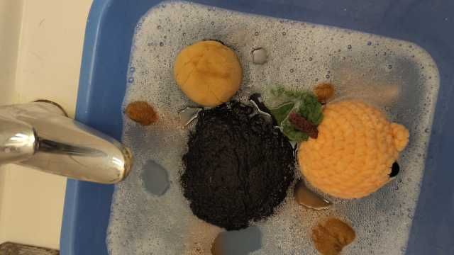 Wolle (das Plüschschaf) und Petunia (der Pfirsichwal) liegen im Wasser in der blauen Schale. Wolle liegt auf dem Rücken.