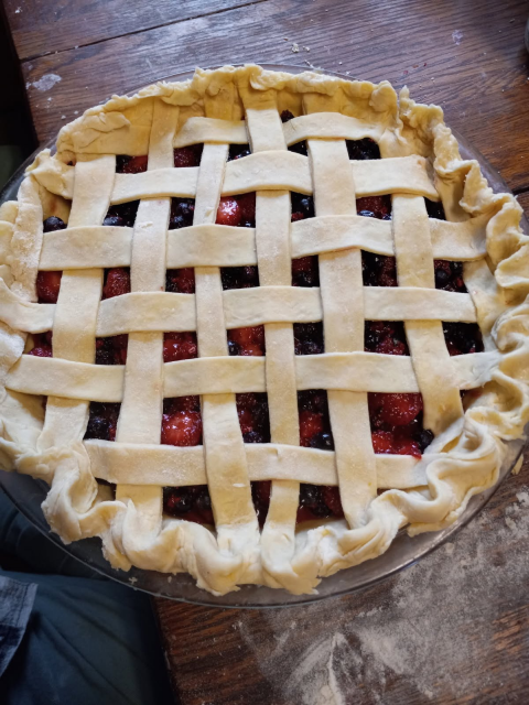 A close up photo of an unbaked lattice-top pie sitting on a flour-covered wooden table.  It got eaten very quickly after it came out of the oven!  So no after-baking picture.
