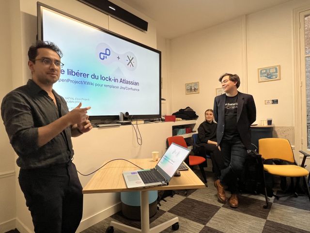 A photo of Parimal Satyal presenting during an OpenProject and XWiki session in Paris, with Clément Aubin standing beside him and Rosanna Sibora seated in the audience. The slide on the screen discusses freeing organizations from Atlassian lock-in.