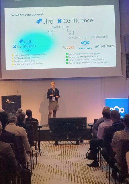 Birthe Lindenthal, Co-founder and CMO of OpenProject, speaking on stage at the Nextcloud Summit 2026 in Munich. Her presentation focuses on open source alternatives to proprietary project management and collaboration tools, with an audience attending the session.