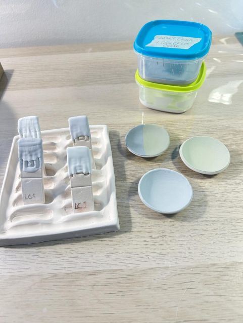 Four white test tiles in a handmade rack and three small shallow bowls in very pale greens and blues