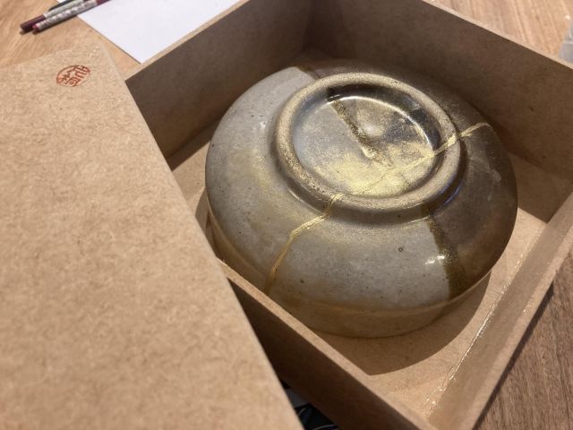 Upside down bowl inside a wooden box with a thin golden line running through the bowl.